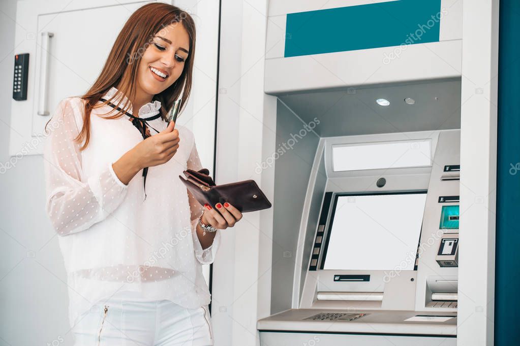 Attractive young woman withdrawing money from credit card at ATM - Image