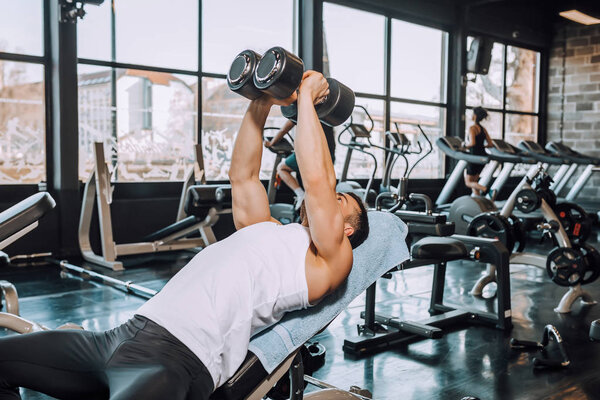 Young attractive adult man exercising and doing weight lifting at fitness gym. Sport training indoors. - Image