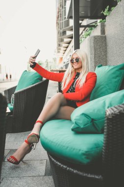 Çekici genç kadın bir akıllı telefon kullanarak ve bir sokak kafe - görüntü istirahat ederken gülümseyen selfie yapıyor