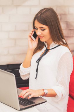 Bir dizüstü bilgisayarda çalışarak ve cep telefonunu bir kafede - görüntü konuşurken çekici genç kadın