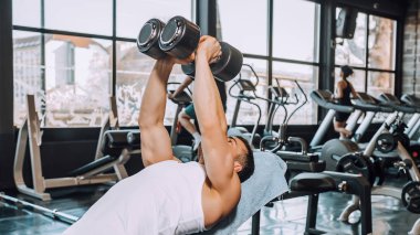 Kaslı adam bir spor salonunda dumbbells ile egzersizleri yapıyor tespit