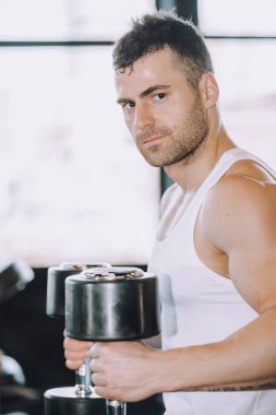 Kaslı vücut geliştirmeci adam spor salonunda dumbbells ile yapıyor 