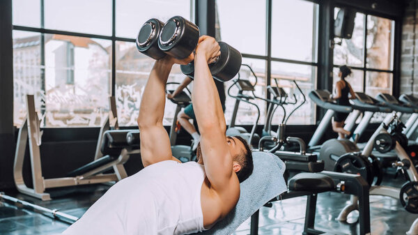 Determined muscular man doing exercises with dumbbells in a gym