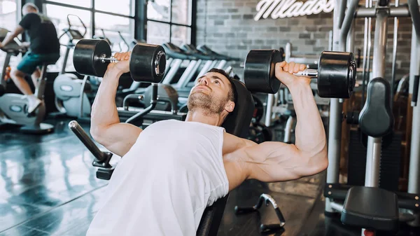 Uomo in allenamento pompare muscoli con manubri in palestra — Foto Stock