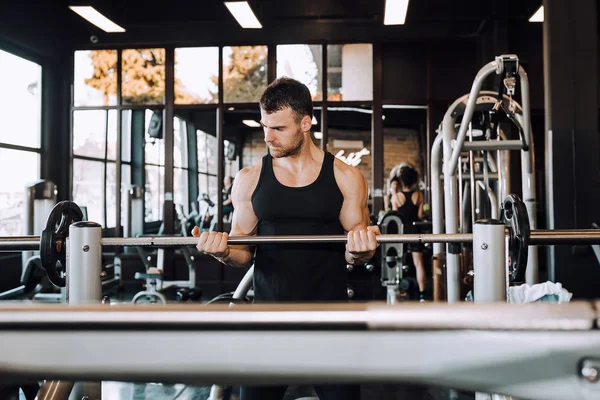 Bir spor salonunda barbell ile kas vücut ile genç adam