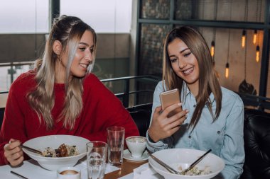 Öğle yemeği sırasında bir cep telefonu kullanarak iki genç kadın