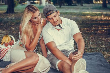 Happx genç çift parkta piknik sırasında akıllı telefon kullanarak