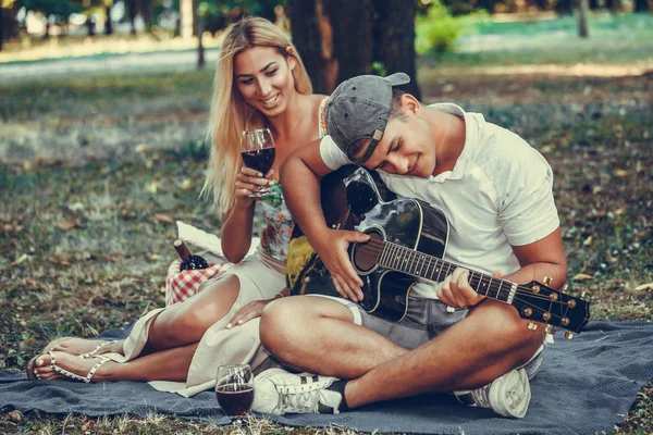 Όμορφο ζευγάρι που διασκεδάζει με την κιθάρα κατά τη διάρκεια του πικ-νικ στο par — Φωτογραφία Αρχείου