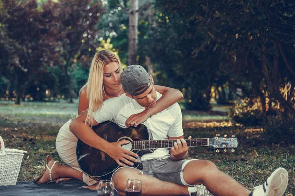 Hermosa pareja joven divirtiéndose con la guitarra durante el picnic en t —  Fotos de Stock