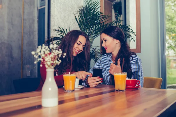 Две возбужденные девушки, сидя в кафе, пользуются мобильным телефоном — стоковое фото