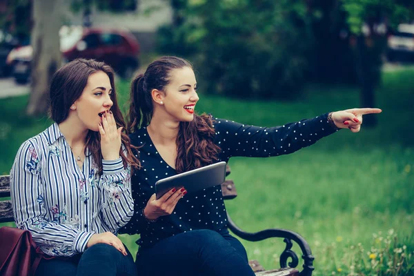 İki güzel kadın sokakta işaret eden bir tablet tutan iki güzel kadın