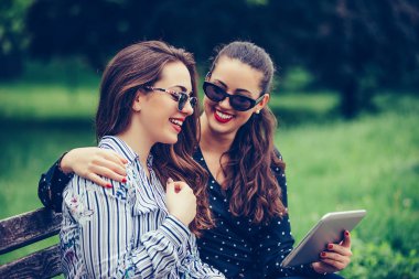 İki güzel kız dijital tablet kullanıyor, konuşuyor, sarılıyor.