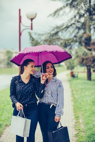 Two female best friend walking in the park with umbrella and poi