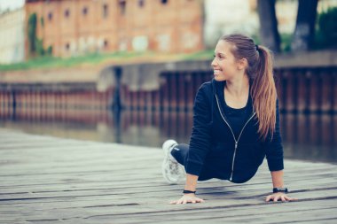 Genç kadın nehir kıyısında şınav çekiyor.