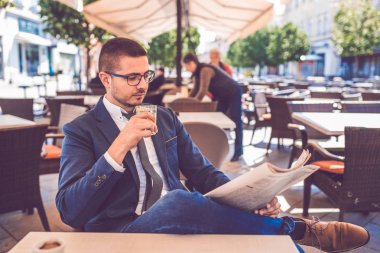 Elinde bir bardak su olan genç adam gazete okuyor