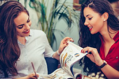 Mutlu kadın arkadaşlar konuşma ve bir kafede dergi okuma