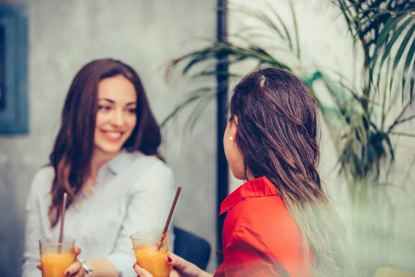 Due giovani donne felici che parlano e bevono succo di frutta fresco in — Foto Stock