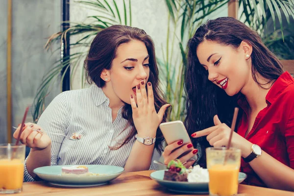 Две молодые женщины едят торты и пользуются телефоном в кафе — стоковое фото