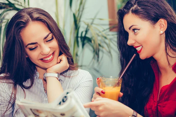 Две молодые женщины разговаривают и читают журнал в кафе — стоковое фото