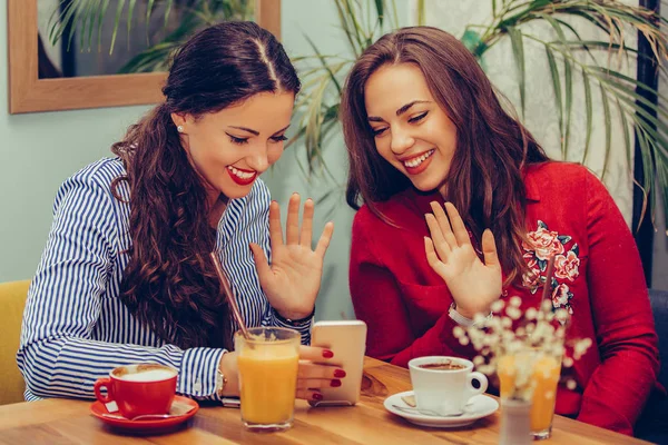İki genç kadın el sallayarak ve bir video cal sahip iken konuşurken