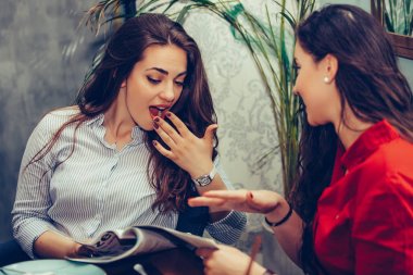 İki şaşırmış genç kadın konuşurken ve okurken kahve içiyor