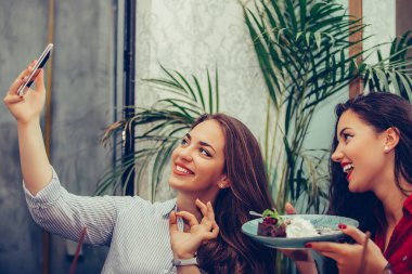  İki genç kadın pasta yiyor ve akıllı telefonla selfie çekiyor 