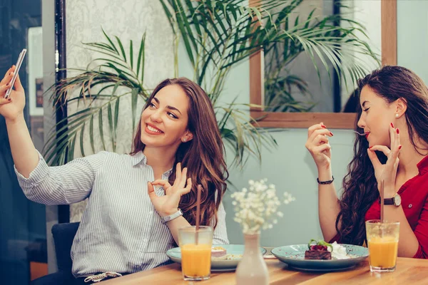 Две молодые женщины едят торты показывая ОК жест во время принятия se — стоковое фото
