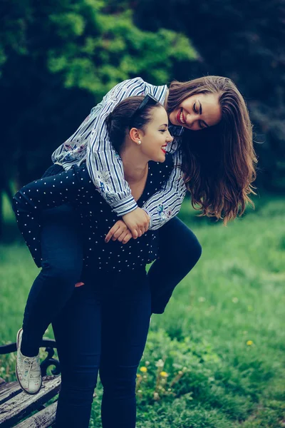 Tiro ao ar livre de jovem mulher carregando seu amigo fêmea em seu ba — Fotografia de Stock