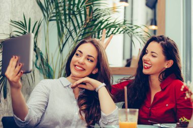 Kafede eğlenen ve sekmeyle selfie çeken iki kadın arkadaş