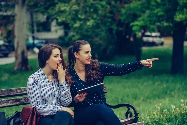 Dos hermosas mujeres sosteniendo una tableta apuntando hacia la calle — Foto de Stock