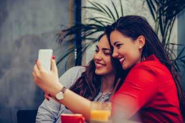 Kafede eğlenen ve smartp ile selfie çeken iki genç kadın