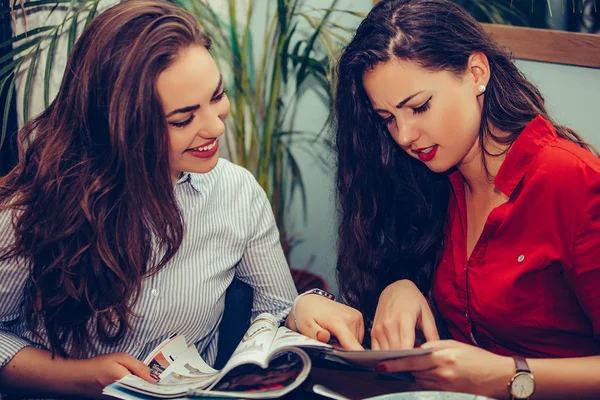 Dos amigas hablando y leyendo revista en un café — Foto de Stock