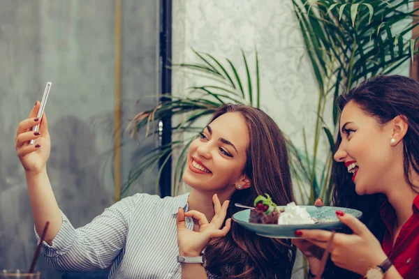 Две молодые женщины едят торты и делают селфи со смартфоном — стоковое фото