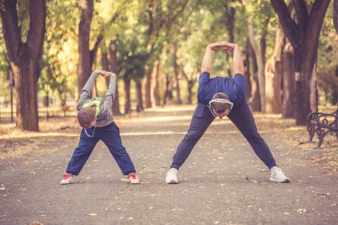 Küçük bir çocuk ve babası birlikte parkta egzersiz