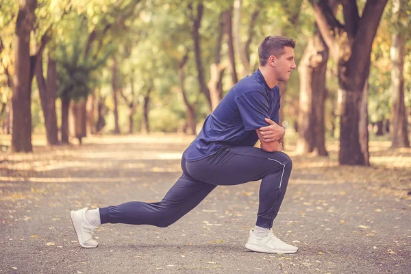 Jovem desportivo homem esticando as pernas no parque se preparando para w — Fotografia de Stock