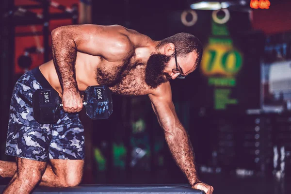 Uomo muscoloso barbuto che lavora in palestra facendo esercizi con du — Foto Stock