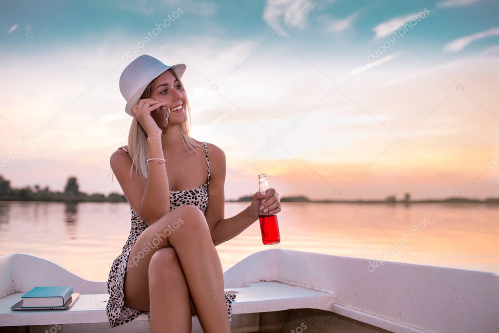 Happy young woman in a dress sitting on the boat and talking wit