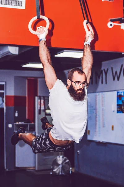 Uomo muscoloso barbuto facendo intenso allenamento sugli anelli di ginnastica — Foto Stock