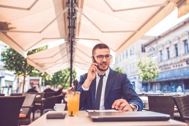 Kahve sırasında gözlüklü genç işadamı telefonda konuşuyor 