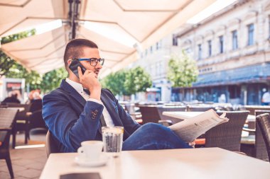 Genç adam gazete eading ve cep telefonu konuşuyor