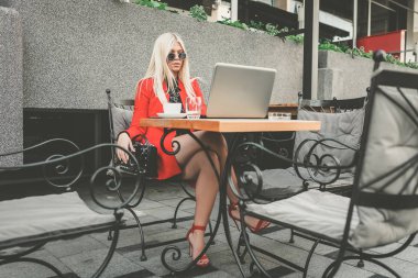 Kafede oturan, kahve içen ve dizüstü bilgisayarla çalışan genç bir kadın.