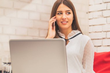 Dizüstü bilgisayarda çalışan ve cep telefonuyla konuşan genç kadın