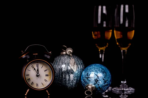 Two wine glasses with champagne, clock and Christmas ornaments