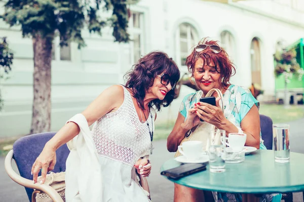 Две сеньорки пьют кофе и пользуются телефоном. — стоковое фото