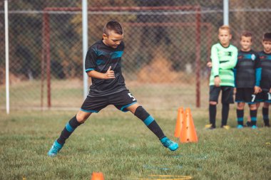Futbol formalı çocuk koni ve ring arasında koşuyor ve zıplıyor. 