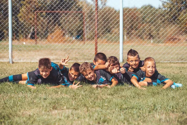 Niños jugadores de fútbol celebrando la victoria juntos mientras yacen en —  Fotos de Stock