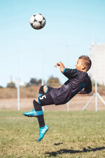 Little boy with soccer ball doing flying kick at stadium.