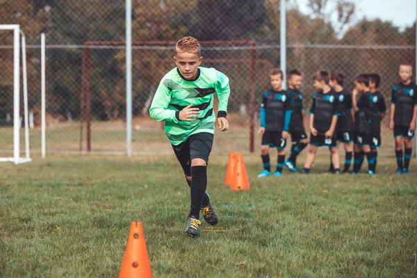 Jovem jogador em camisa de futebol correndo entre cones e ring lad — Fotografia de Stock