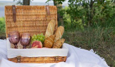 Bir kayanın üzerinde piknik, büyük bir nehrin arka planında, gölde. Güneşli bir günde bir tarlada piknik öğle yemeği. Baget, kruvasan, şeftali, bir buket kır çiçeği ve üzüm..