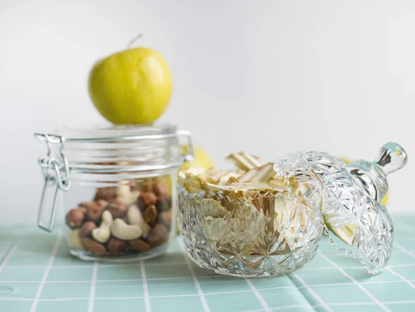 Dried apples, apple chips. Healthy snack, diet. Dried apples in a vintage plate on a turquoise background. Mix of nuts in a glass jar. Cashews, hazelnuts and almonds. Selective focus, copy space.